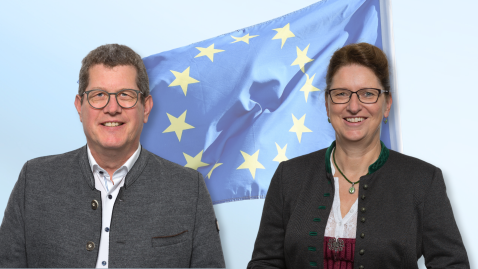 Herr Köhler und Frau Singer stehen vor der EU Flagge